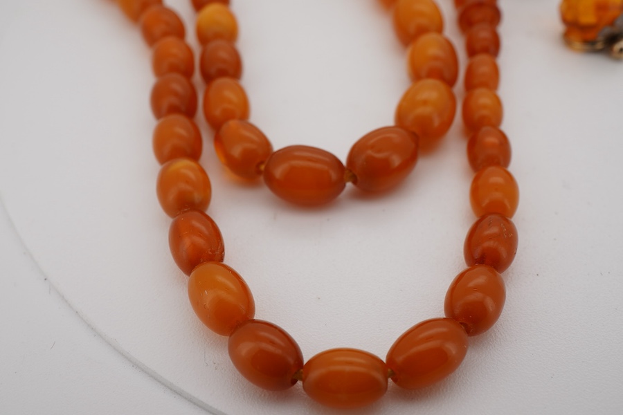 A single strand graduated oval amber bead necklace, 40cm, gross weight 9 grams, together with an amber cluster set brooch and pair of earrings.